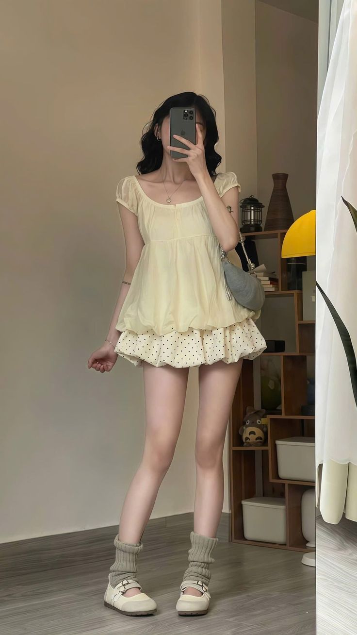 Woman in a yellow top and polka dot skirt taking a mirror selfie