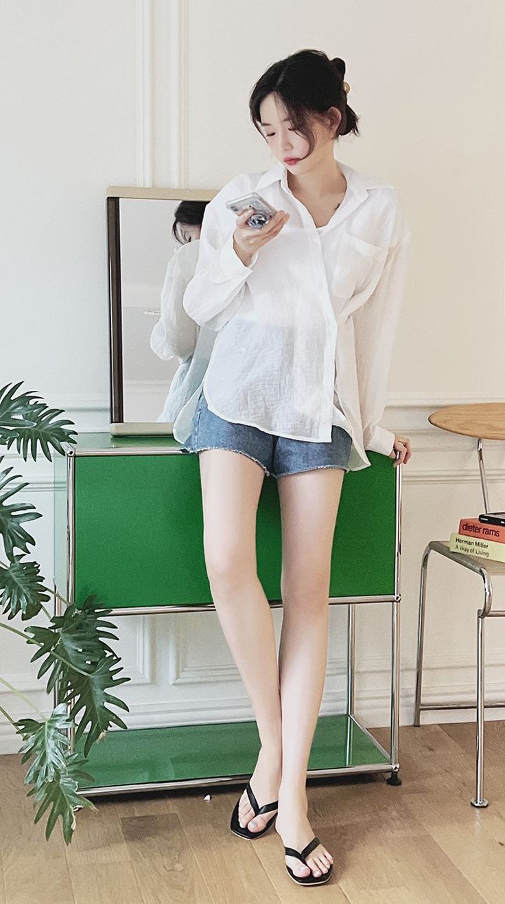 Woman in a white shirt and denim shorts looking at her phone indoors