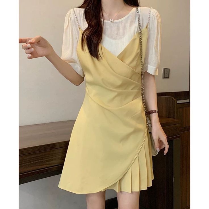 Woman in a yellow dress over a white shirt, holding a shoulder bag indoors