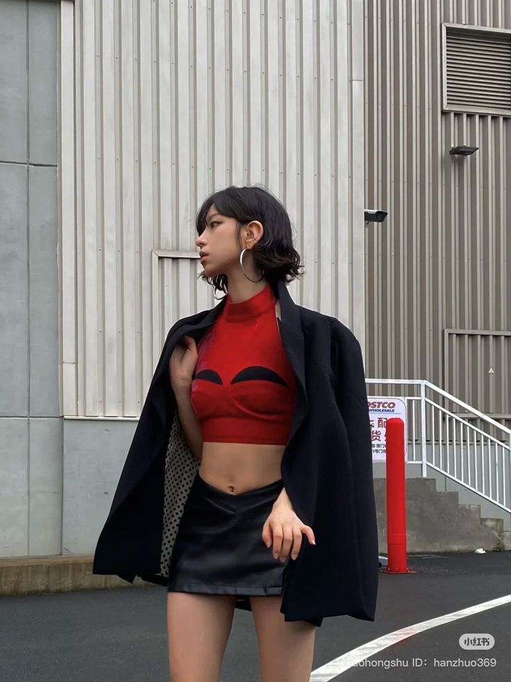 Woman in a red crop top and black mini skirt with a blazer over her shoulders