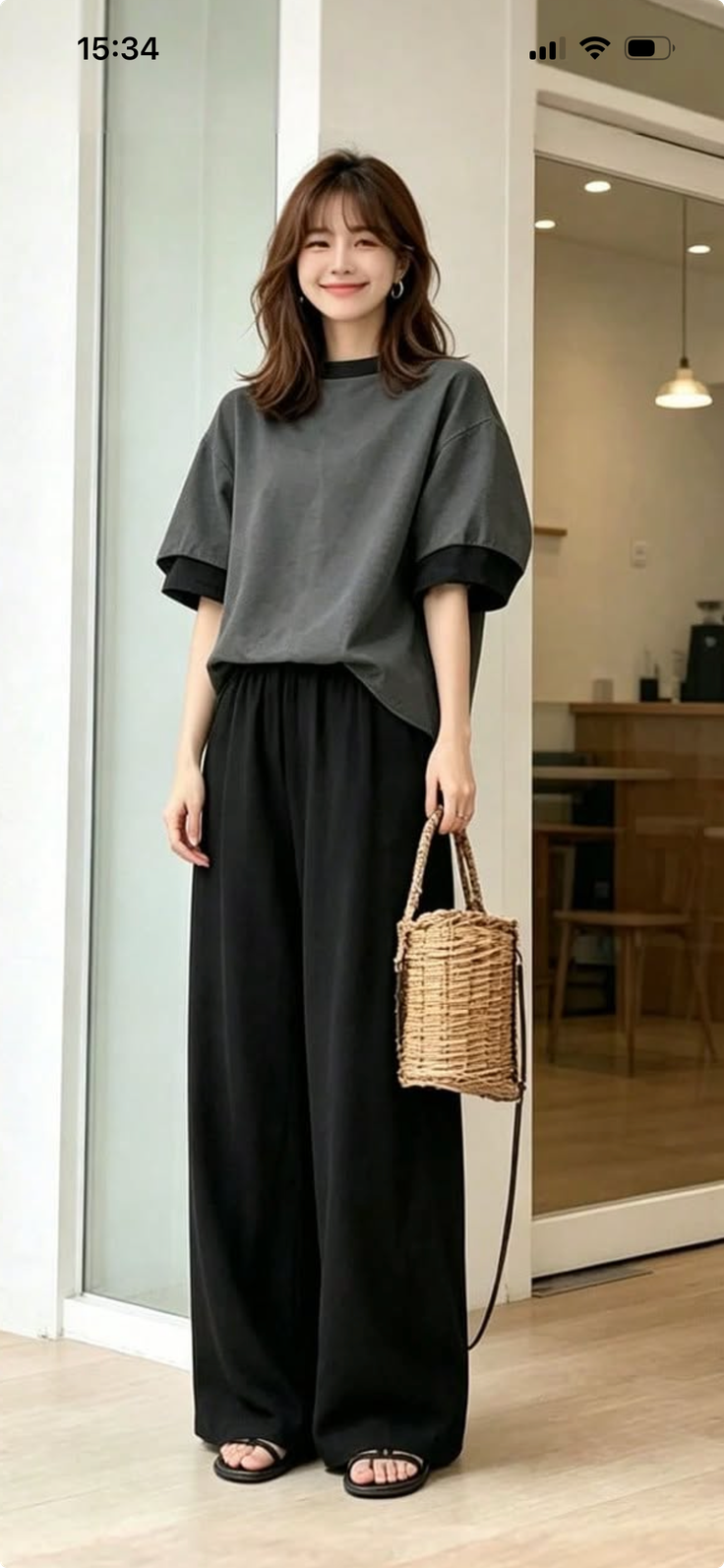 Woman with long hair wearing a t-shirt and wide leg pants, holding a straw bag