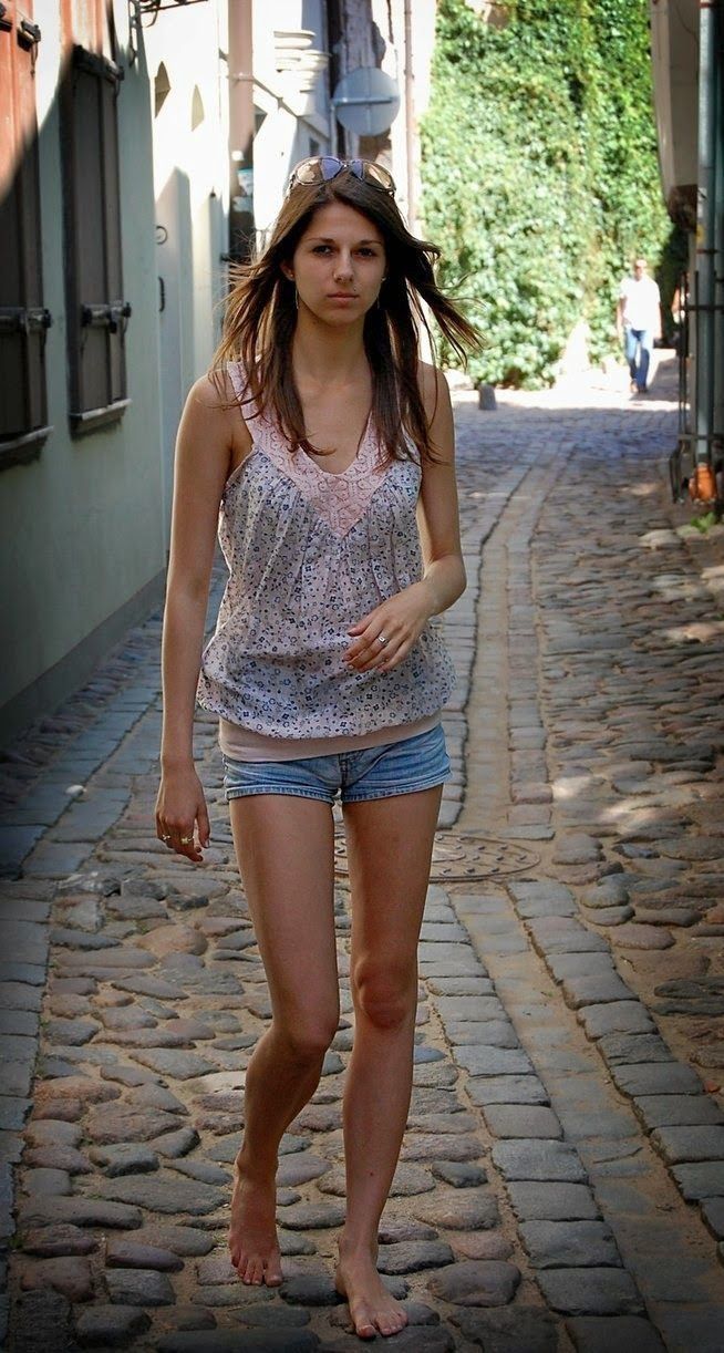 Young woman with long hair walking barefoot on a cobblestone street