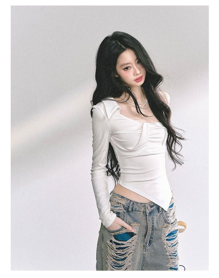 Woman with long black hair wearing a white top and ripped jeans indoors