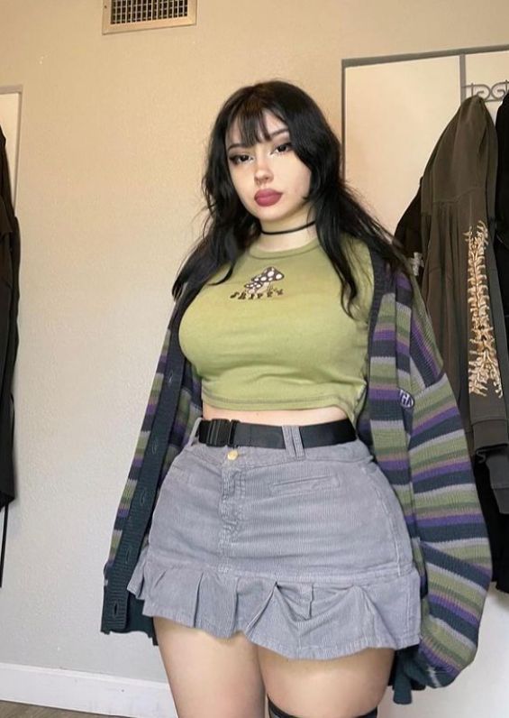 Woman with long black hair and bangs wearing a cropped top and mini skirt indoors
