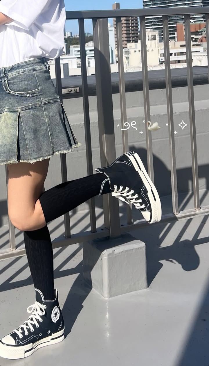 Person in a denim skirt and high top sneakers on a rooftop