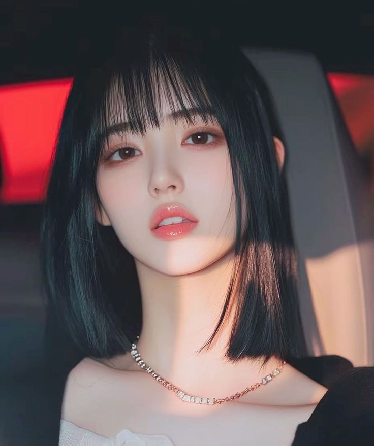 Woman with short black hair and bangs wearing a necklace, with warm lighting