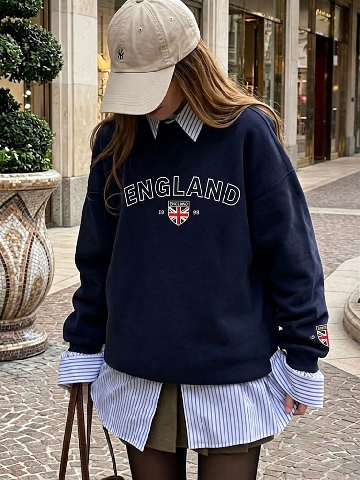 Person wearing a navy sweatshirt and baseball cap over a striped shirt outdoors