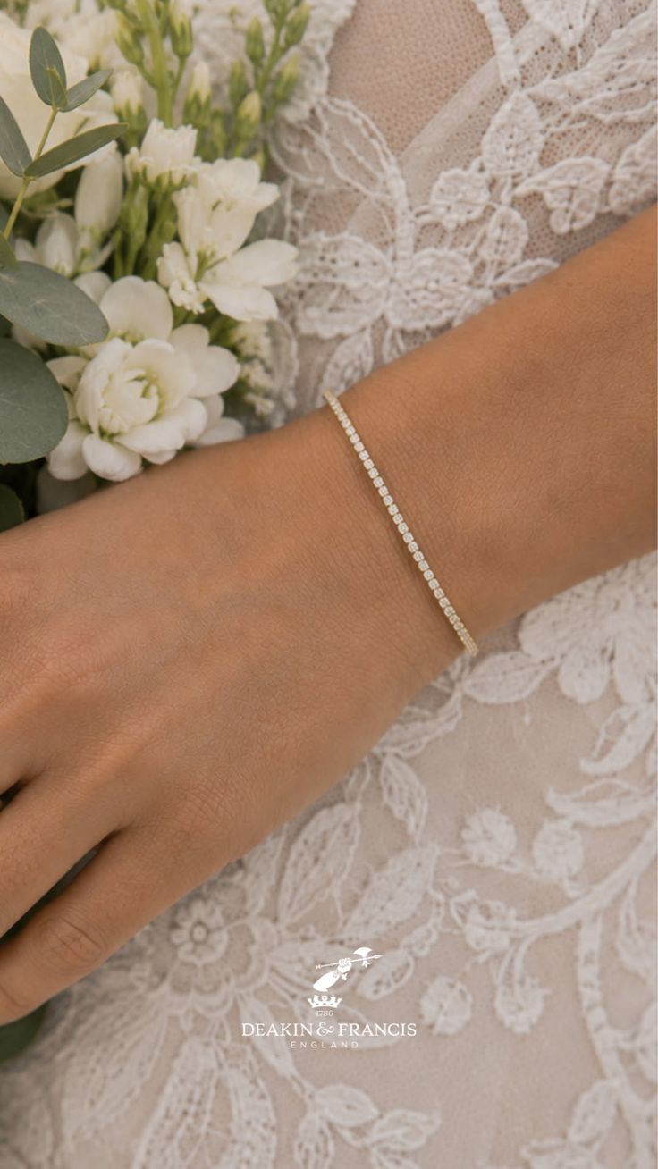A woman's arm wearing a diamond bracelet, holding a white wedding bouquet