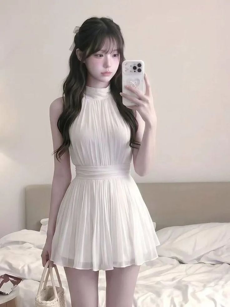 Woman in a white dress taking a mirror selfie in a bedroom