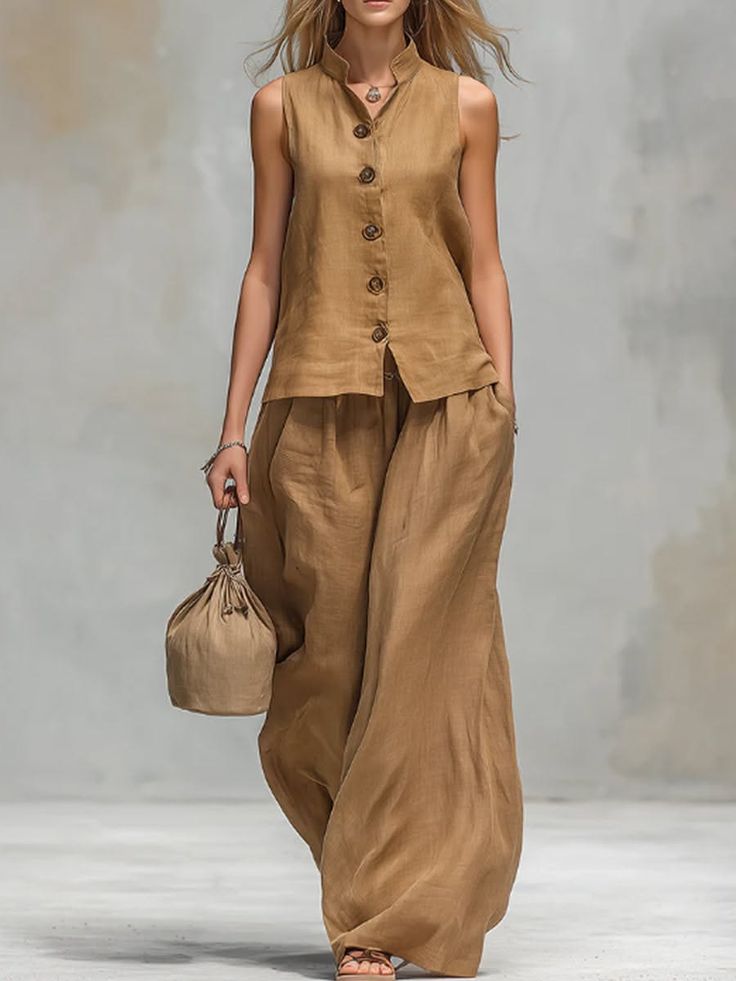 Woman in a brown linen sleeveless top and wide leg pants holding a small bag