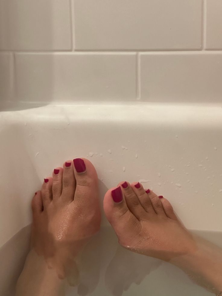 Feet with red nail polish soaking in a bathtub
