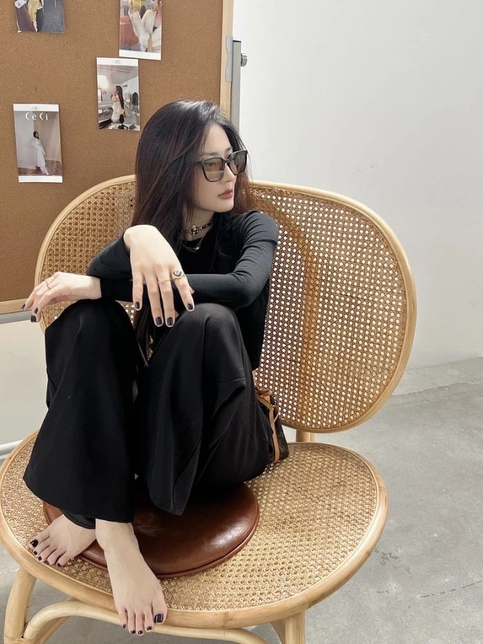Woman with long dark hair and sunglasses sitting on a wicker chair indoors