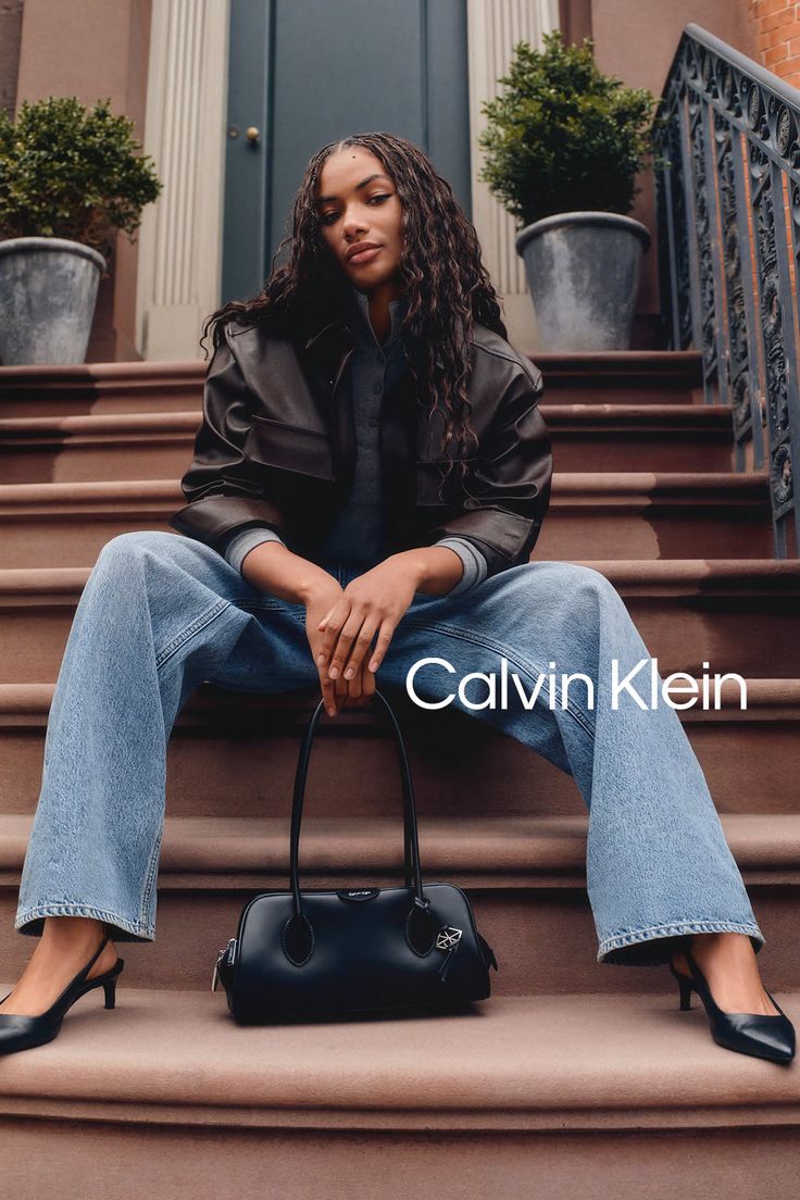 Woman with long hair sitting on outdoor steps, wearing a leather jacket and jeans