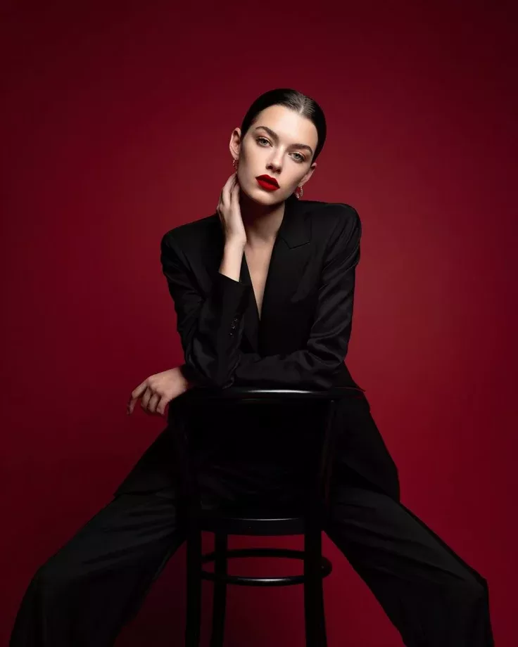 Woman in a black suit with red lipstick posing against a red background
