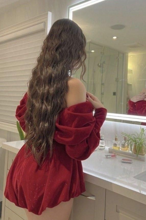 Woman with long wavy hair in a red off-shoulder dress in a bathroom