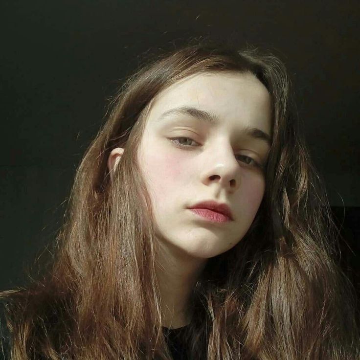 Young person with long brown hair in soft lighting against a dark background