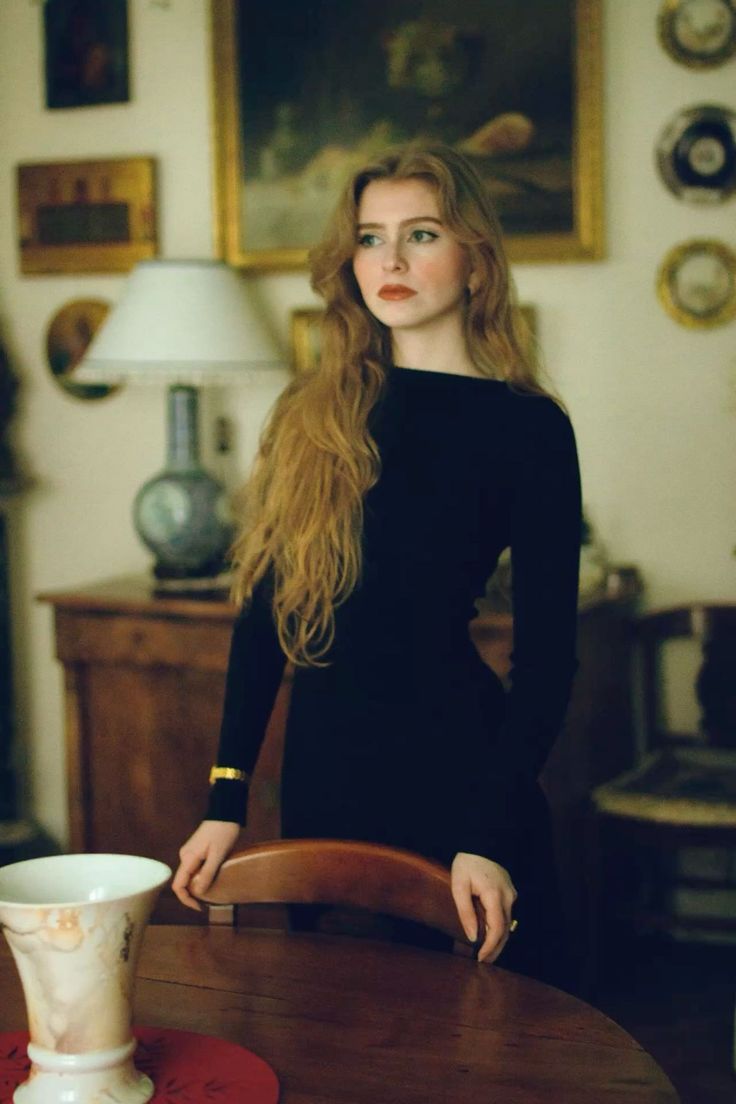 Woman with long red hair in a black dress standing indoors