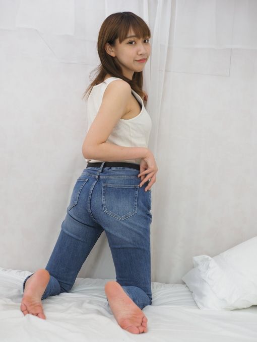 Woman in blue jeans and a white tank top kneeling on a bed