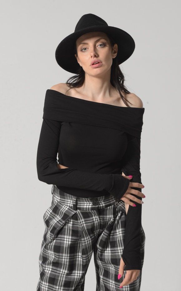 Woman in a black off-shoulder top and plaid pants with a black hat
