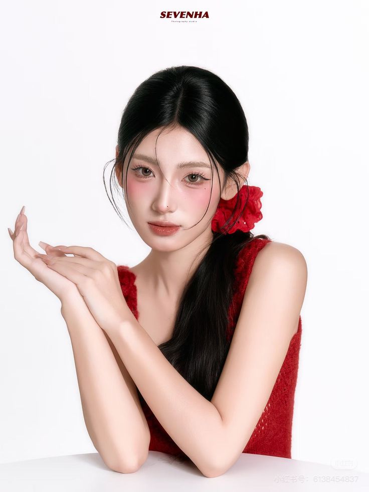 Woman with black hair in a ponytail and a red top against a white background