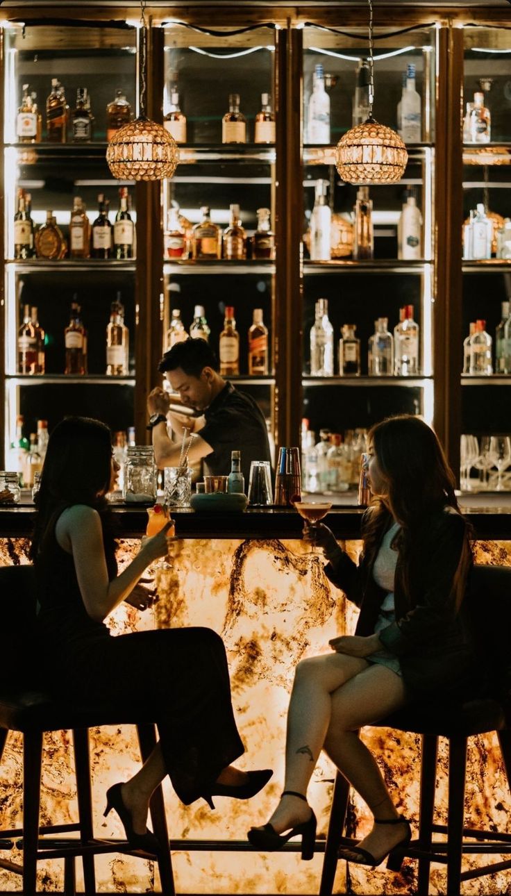 Two women drinking cocktails at a bar with a bartender in the background