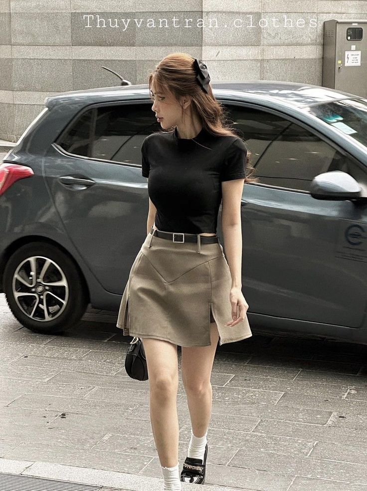 Woman in a black top and mini skirt walking on a street next to a car