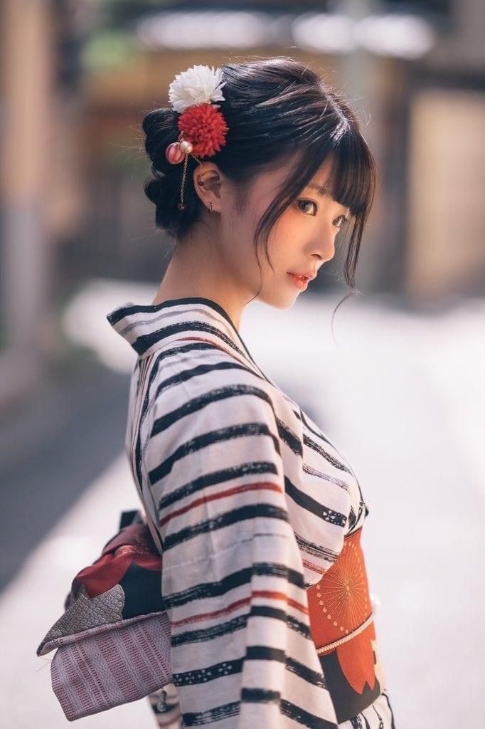Woman in a striped kimono with a floral hair ornament looking to the side