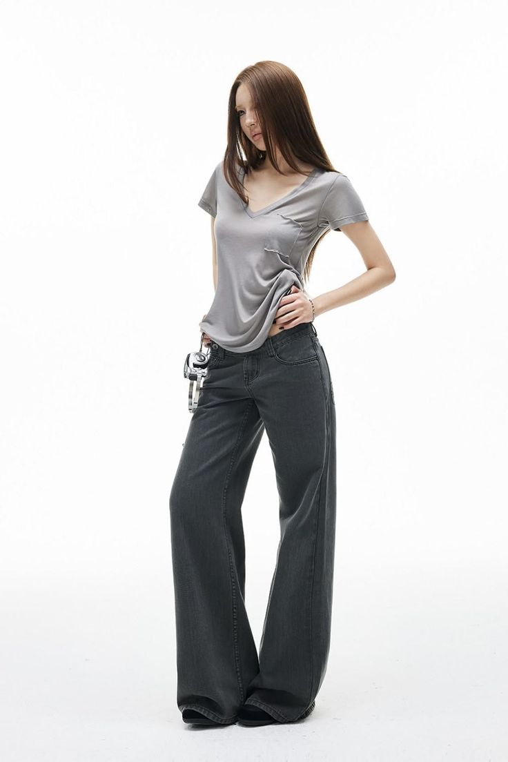 Woman with long hair in a gray t-shirt and wide leg jeans on a white background