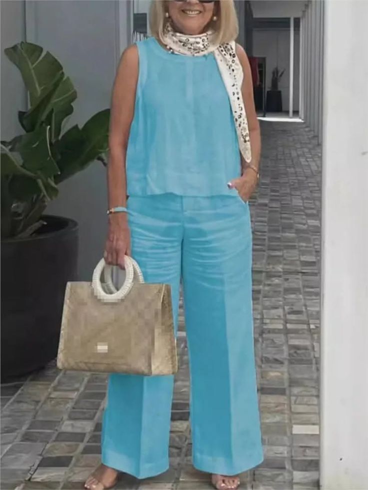 Woman in a blue sleeveless top and wide leg pants holding a handbag