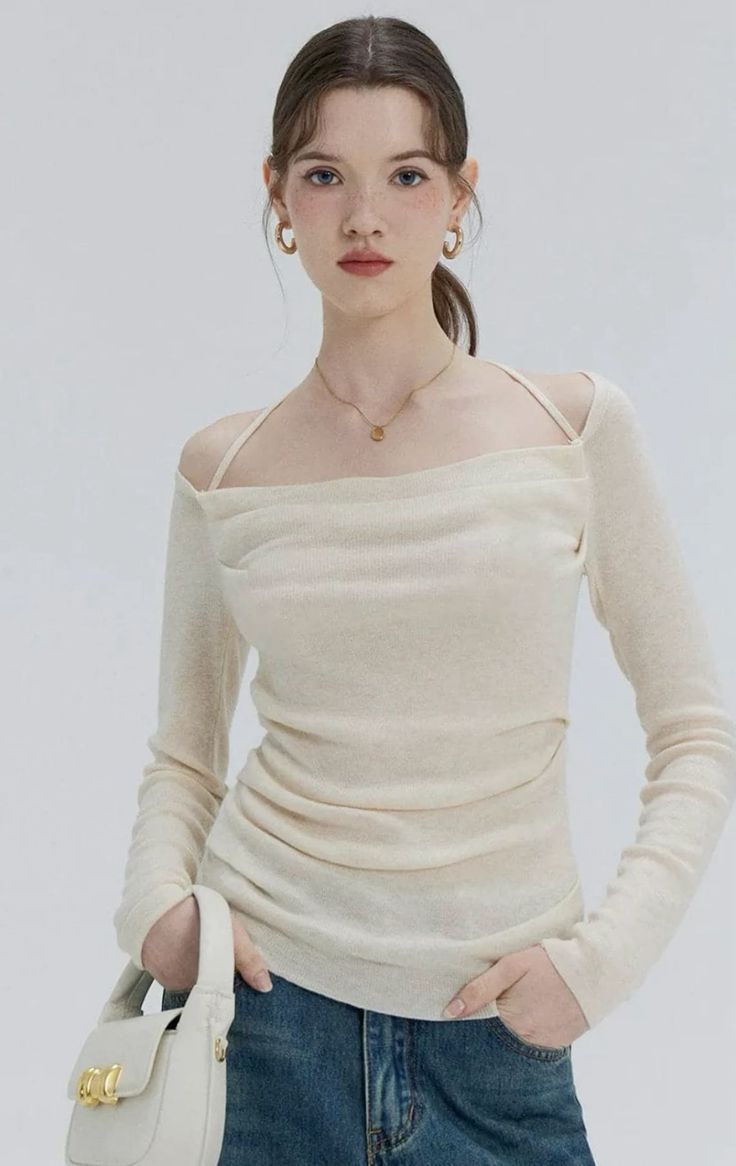 Woman in a cream long sleeve top and blue jeans holding a white shoulder bag