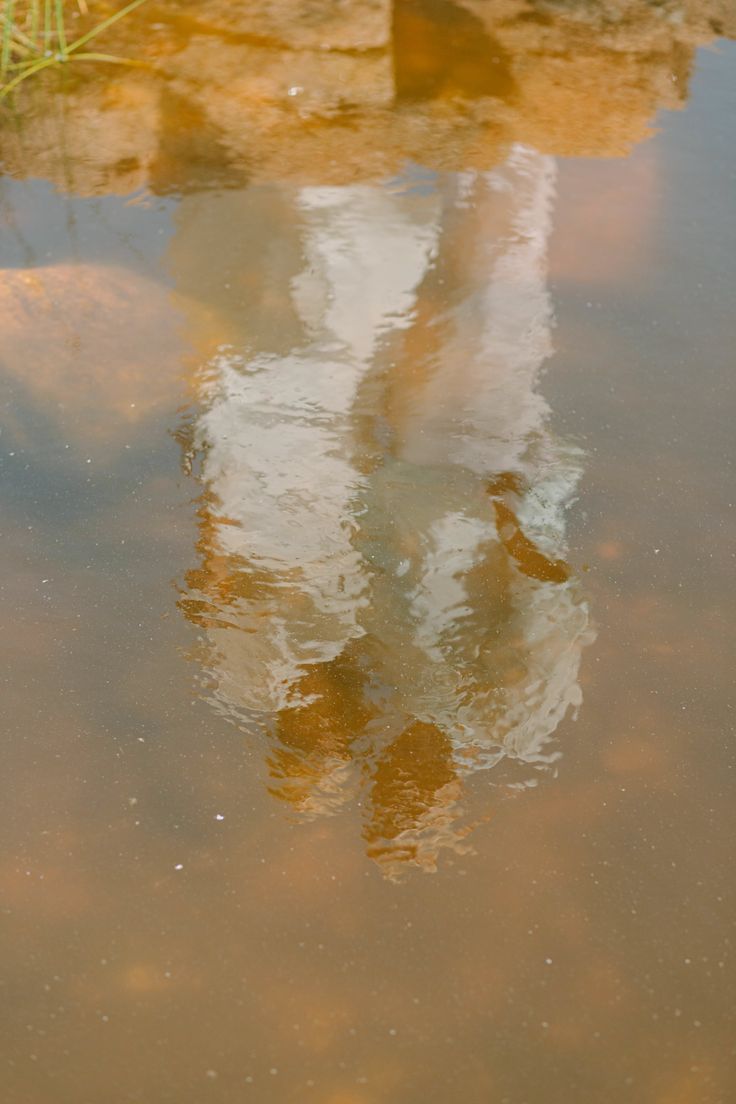 Distorted reflection of a person in brown water with ripples