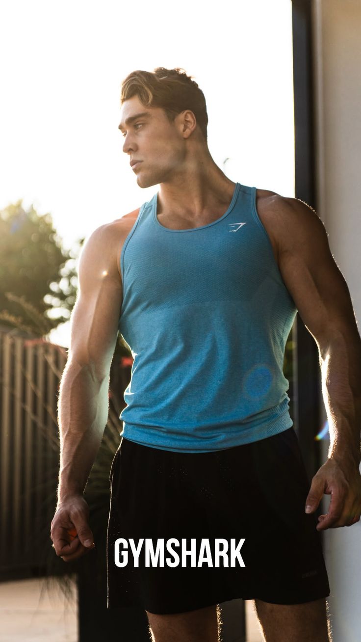 Muscular man in a blue tank top and black shorts outdoors with backlight