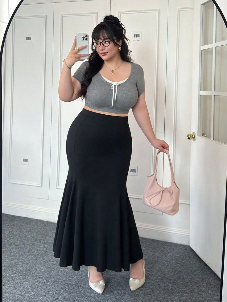 Woman with black hair and glasses taking a mirror selfie in a crop top and long skirt