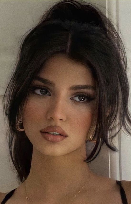 Woman with dark hair in a ponytail and makeup, wearing earrings and a necklace