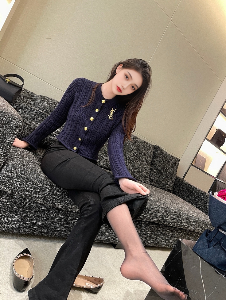 Woman in a dark blue cardigan and black pants with sheer stockings, sitting indoors