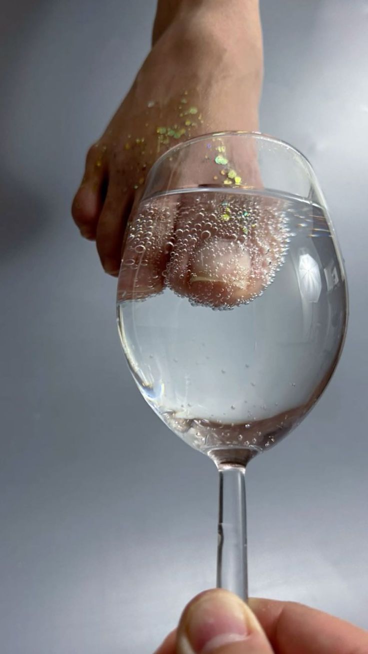 Foot with glitter submerged in a glass of clear liquid with bubbles