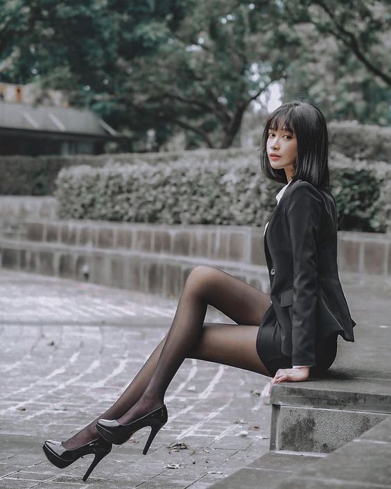 Woman in a black blazer and tights sitting outdoors