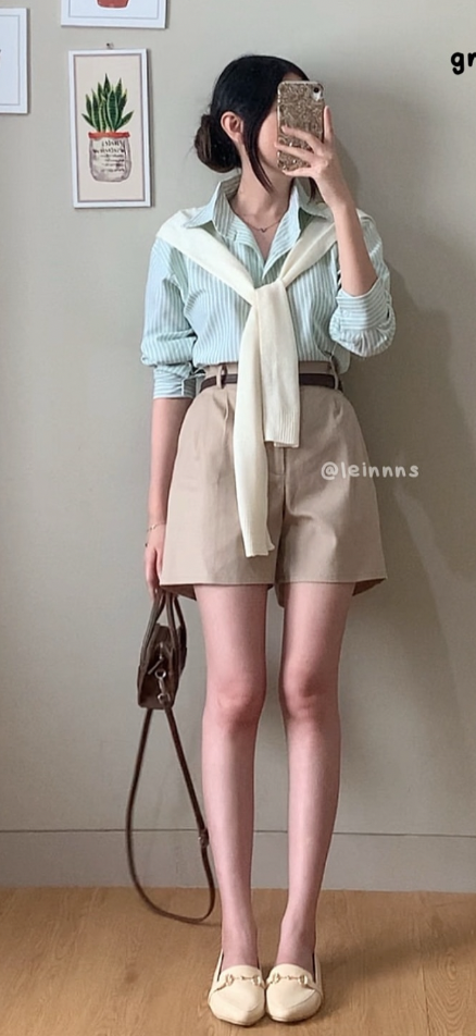 Person in a striped shirt and beige shorts with a sweater tied over shoulders