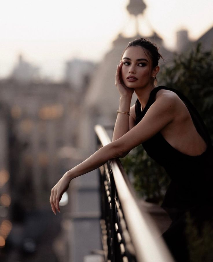 Woman in a black dress leaning on a balcony railing overlooking a cityscape