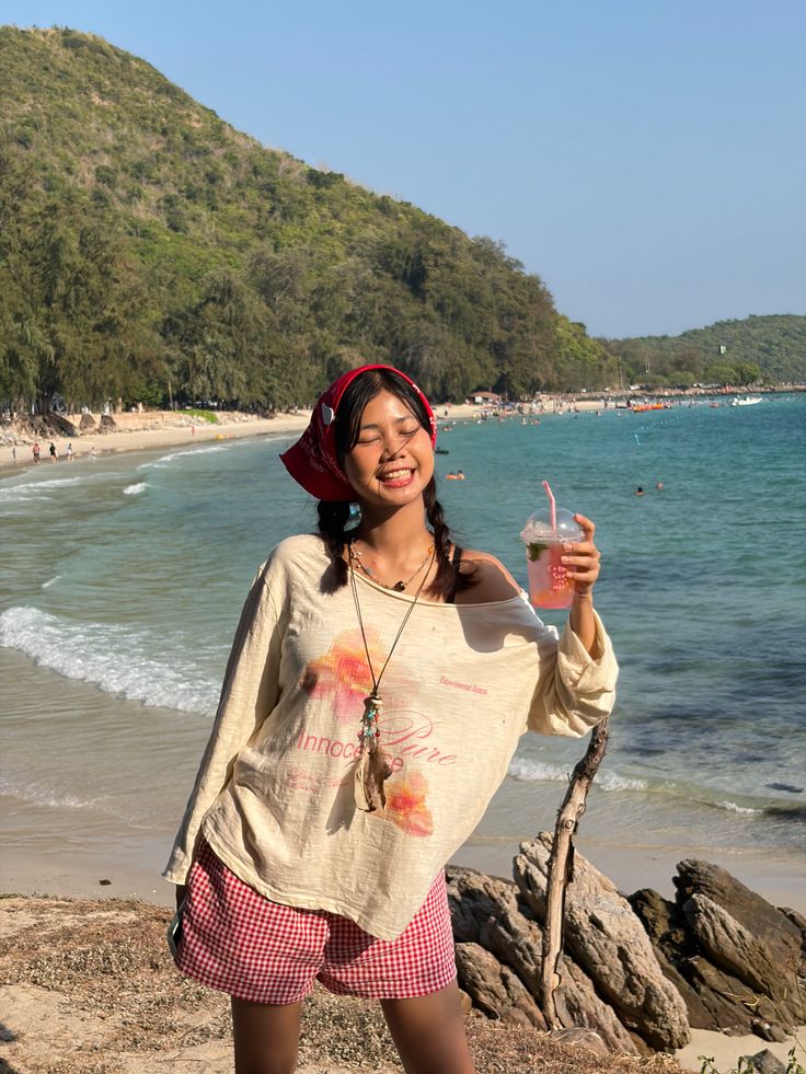 Woman in a red bandana and gingham shorts holding a drink on a sunny beach