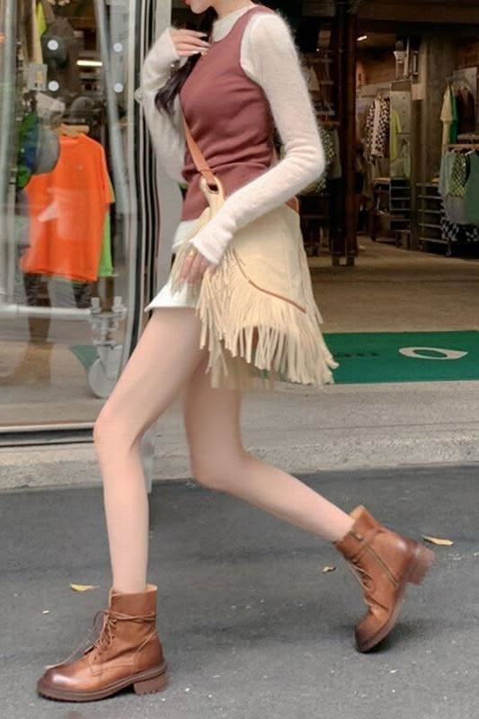 Person in a fringe skirt and brown boots walking on a street