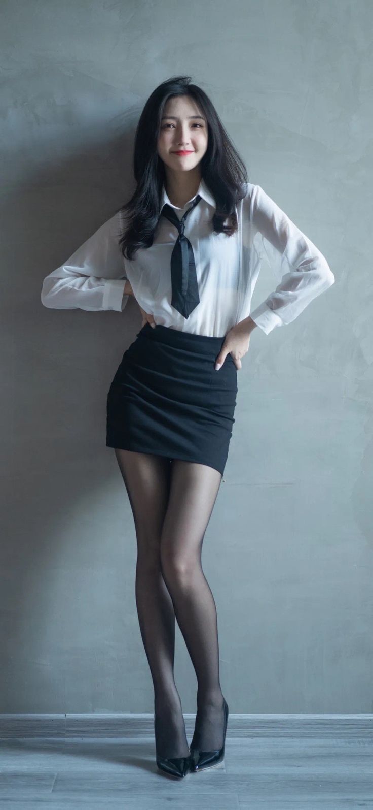 Woman in a white shirt, black tie, mini skirt, and pantyhose posing indoors