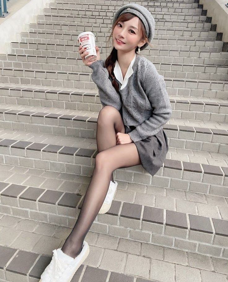 Woman in a beret and cardigan sitting on outdoor stairs, holding a cup