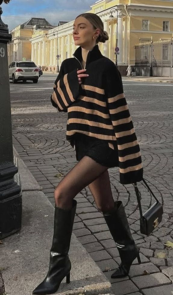 Woman in a striped sweater and black boots walking on a cobblestone street