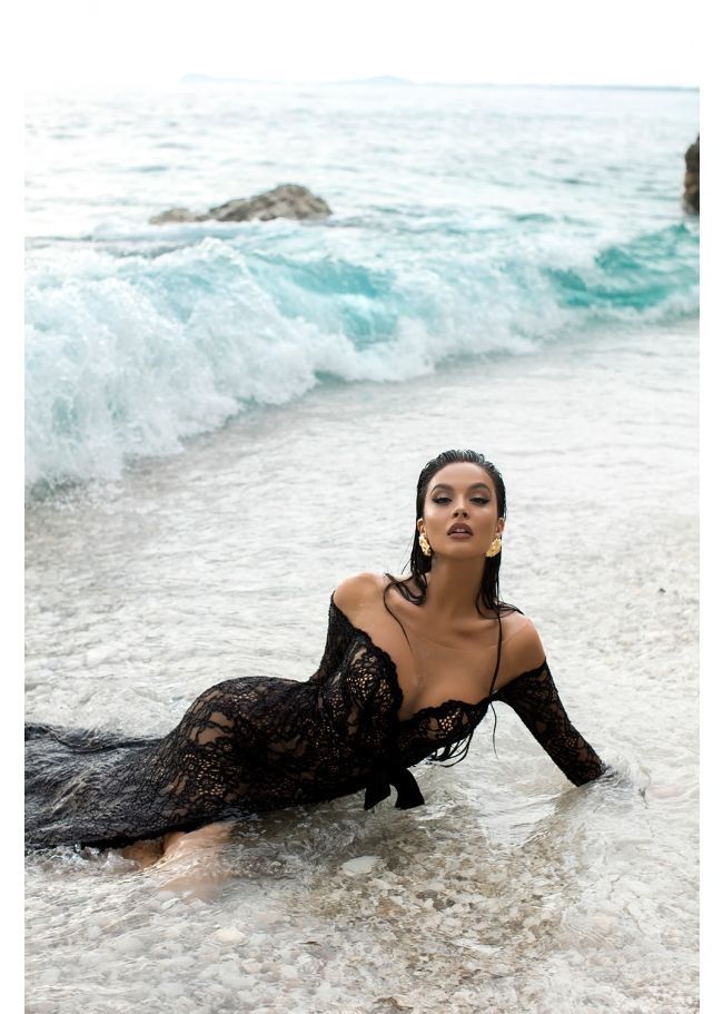 Woman in a black lace dress lying in shallow ocean water with waves