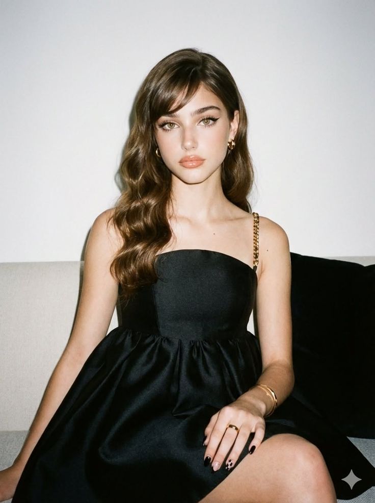 Woman with long wavy hair wearing a black dress and gold jewelry indoors