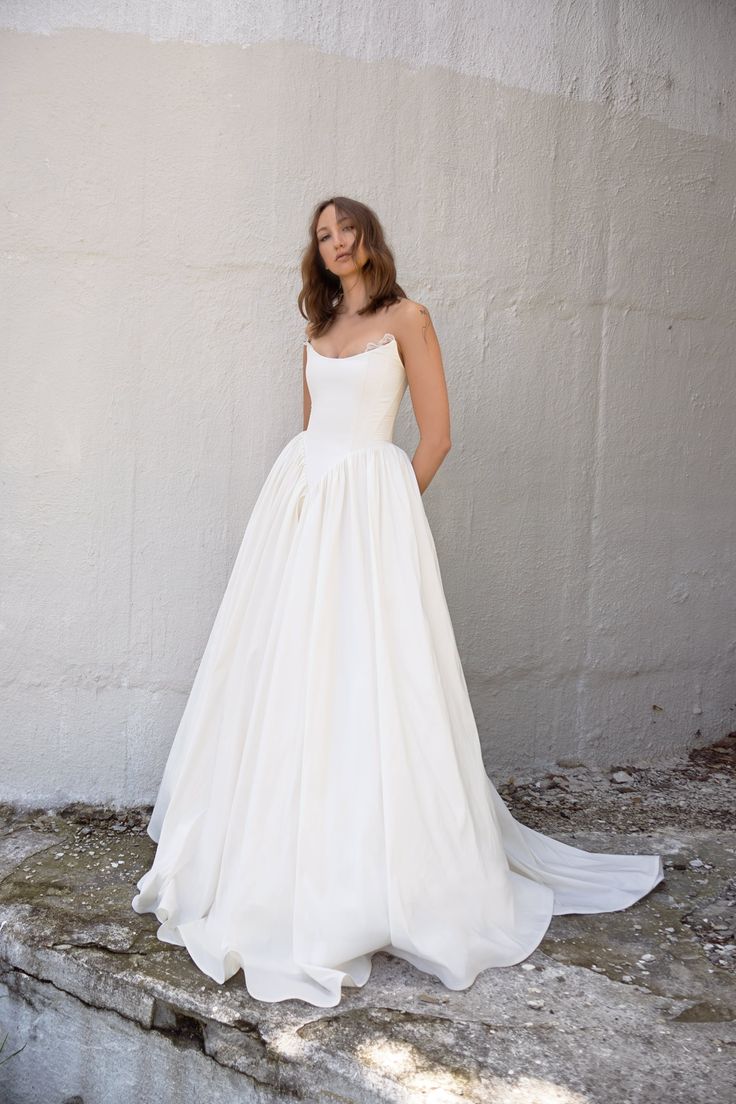 Woman in a white strapless wedding dress standing against a concrete wall