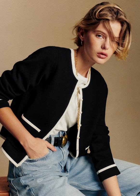 Woman with short blonde hair wearing a black cardigan and jeans