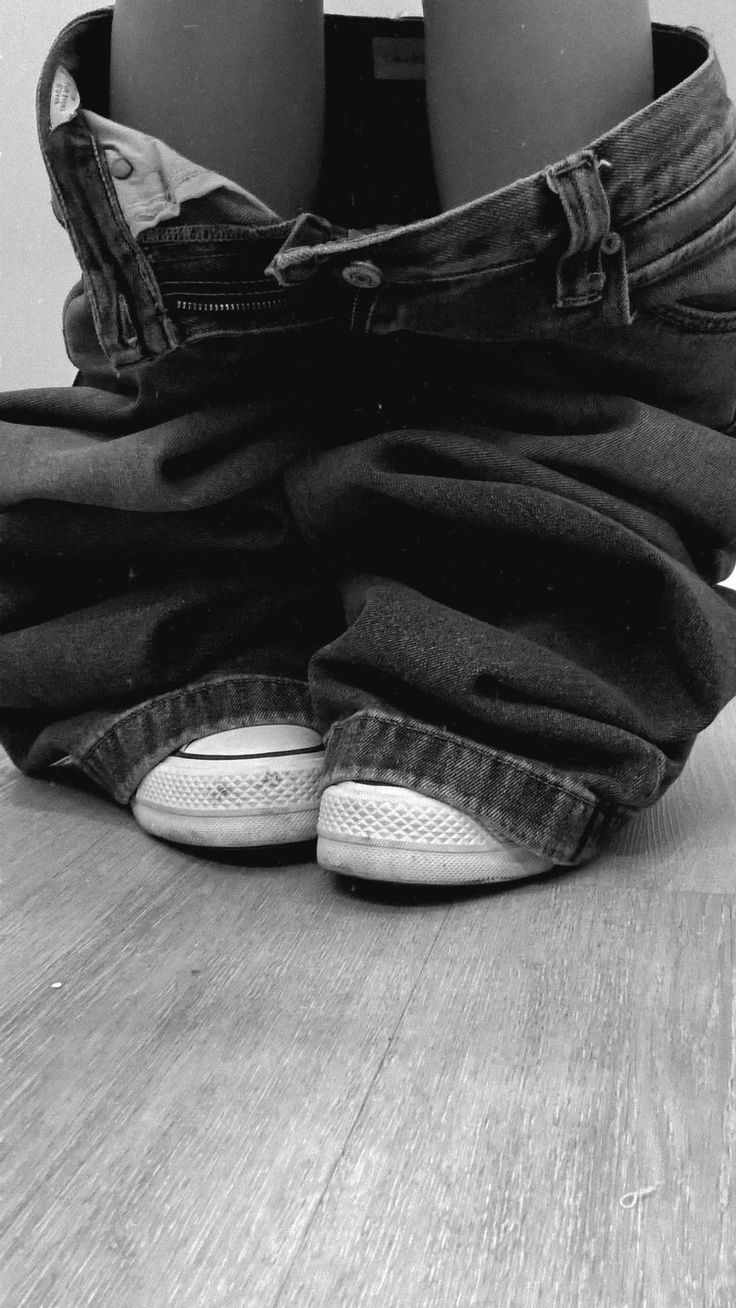 Person with jeans around their ankles and sneakers on a wooden floor