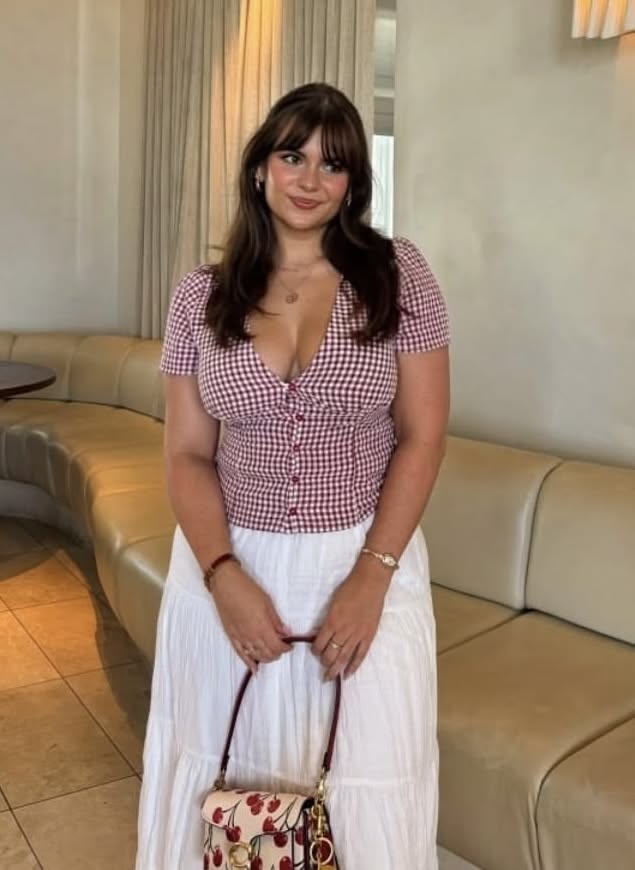 Woman in a red gingham top and white skirt holding a cherry print bag indoors